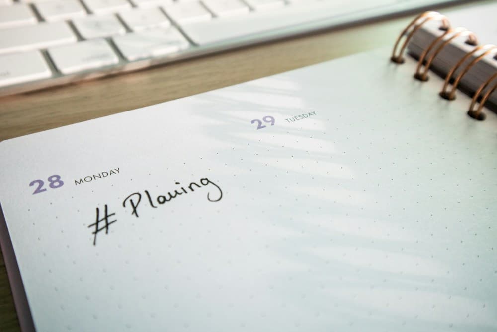 An open weekly planner beside a keyboard, photographed by Walls.io